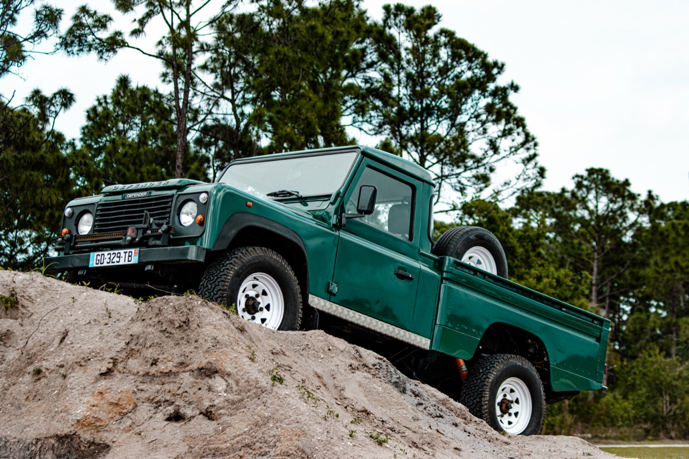 Green Land Rover Defender 110 pick-up articulating over a sand mound